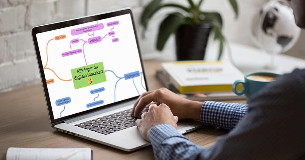 En person lager et digitalt tankekart på en laptop som står på en pult.